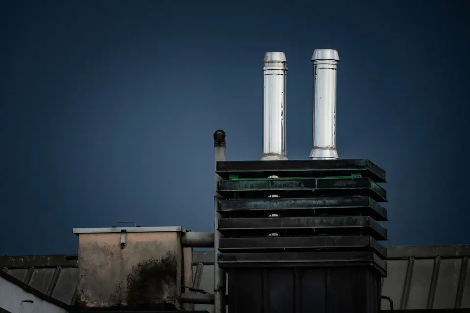 Conduits de cheminée métalliques dressés sur un toit, sous un ciel sombre
